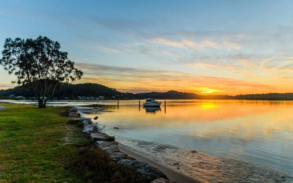 Sunset over Woy Woy waterfront with a moored boat and calm estuary waters